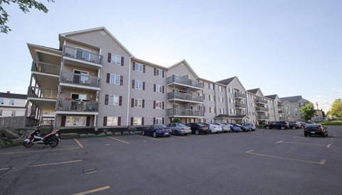 A parking lot with cars and a motorcycle in front of apartment buildings.