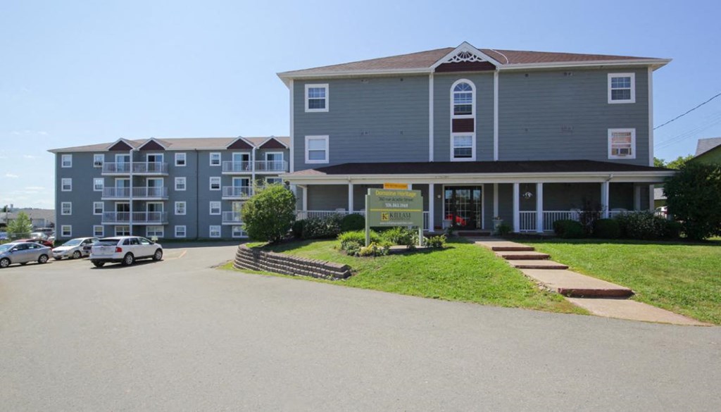 A large grey building with a red roof and a sign in front.