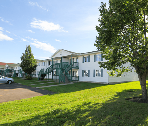 A white building with green railings and a tree in front.