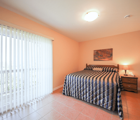 A bedroom with a bed, nightstand, and window with blinds.