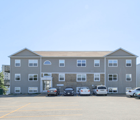 A grey building with a parking lot in front of it.