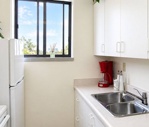 A kitchen with a white fridge, white cabinets, and a window.