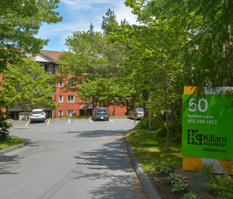 A green and yellow sign for Killam Apartment Rent is on the side of a road.