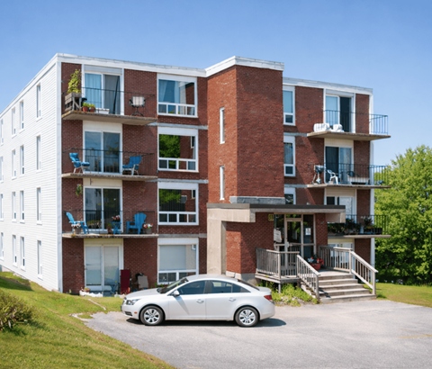 A white car is parked in front of a red brick apartment building.