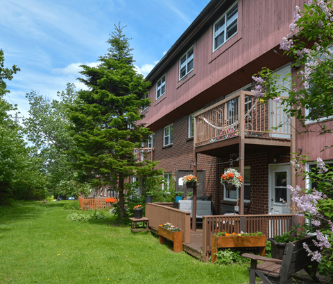 A red building with a balcony and a green lawn in front.