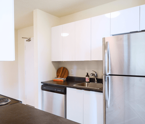 A kitchen with a stainless steel refrigerator and black countertop.