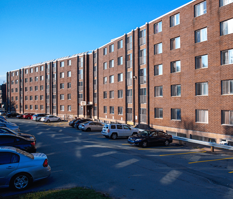 A parking lot in front of a red brick building with cars parked.