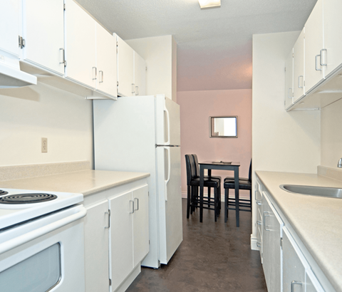 A kitchen with white cabinets and a pink wall.