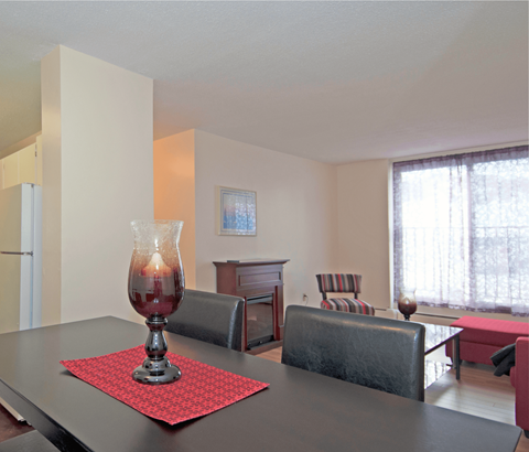 A dining table with a red placemat and a glass vase with a candle inside.