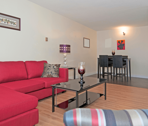 A red couch sits in a living room with a glass table in front of it.