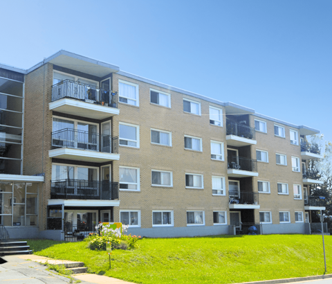 Apartment building with balconies and a green lawn in front.
