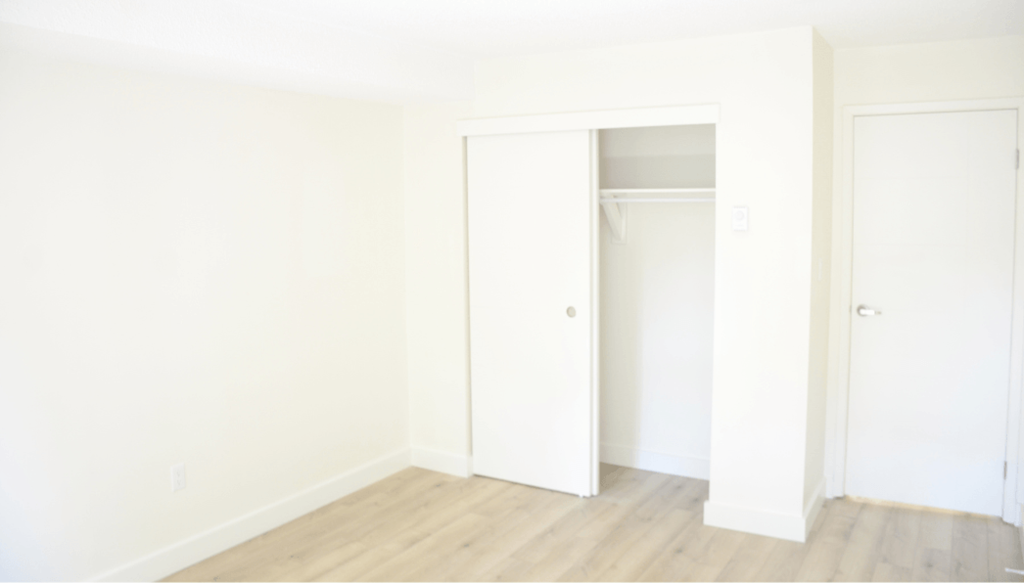 A white room with a door and a shelf.