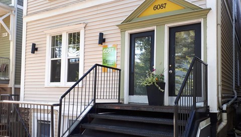 A house numbered 6087 with a black railing and steps.