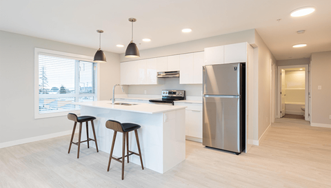 a kitchen with a large island with two stools and a stainless steel refrigerator