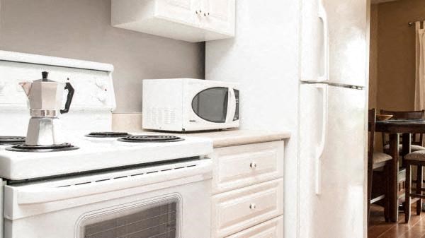 A white stove top oven with a kettle on it and a white microwave above it.