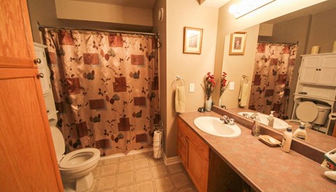 A bathroom with a brown counter top and a shower curtain with a pattern of brown squares and rectangles.
