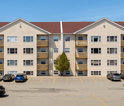 A parking lot in front of a tan apartment building with cars parked.