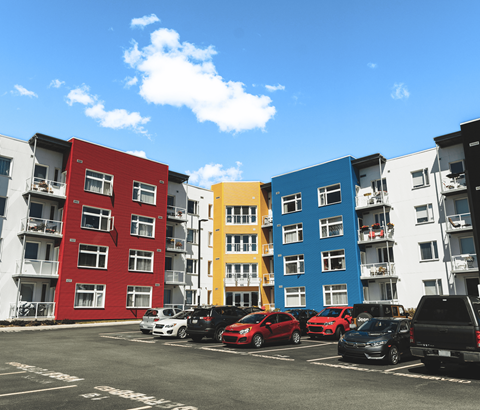 A row of colorful apartment buildings with cars parked in front.