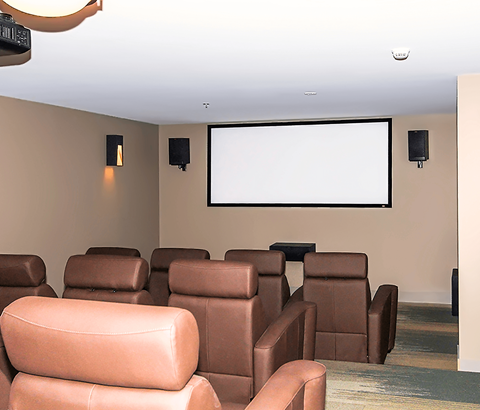 A row of brown leather chairs are arranged in front of a large screen.