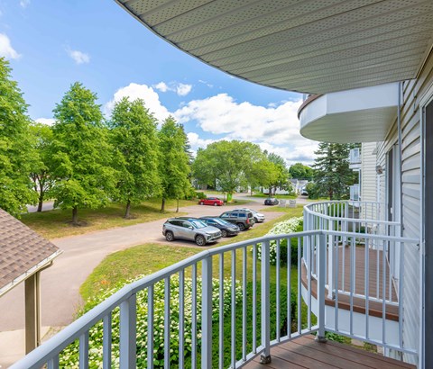 A view from a balcony overlooking a parking lot and trees.