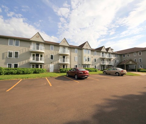 A parking lot in front of a large apartment building with two cars parked.