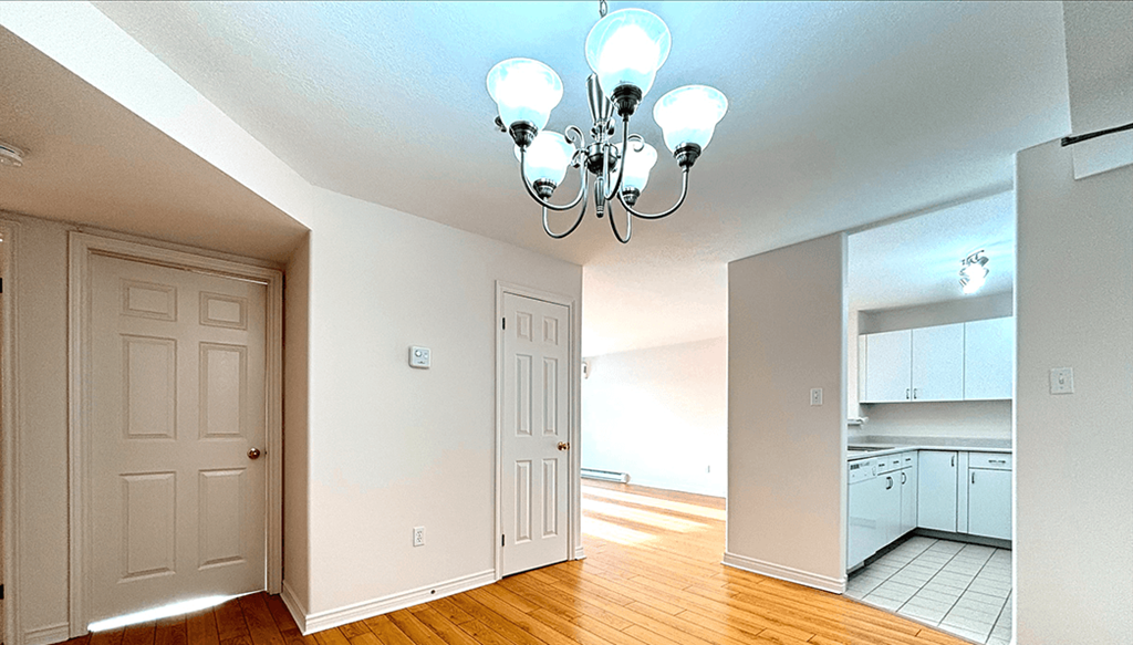 A chandelier hangs over a white door in a room with a kitchen visible in the background.