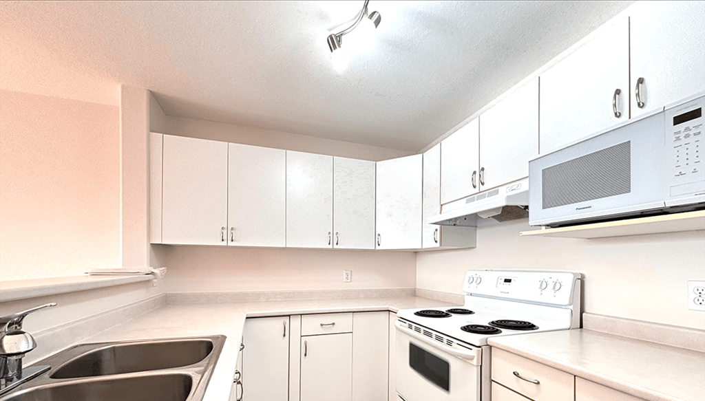 A white kitchen with a sink, stove, and microwave.