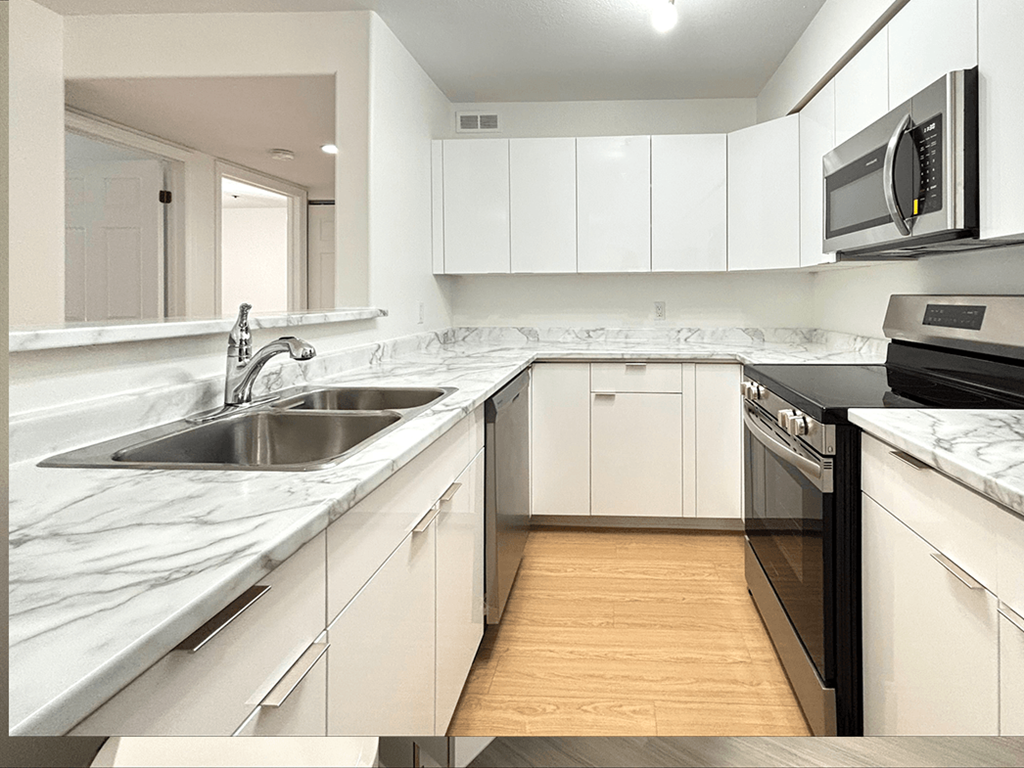 A modern kitchen with white cabinets and a wooden floor.