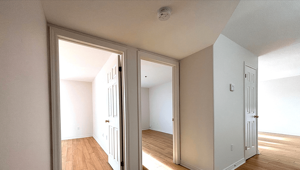 A room with white walls and wooden floors is shown through an open door.