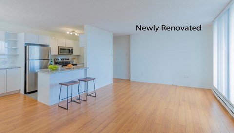 an empty living room with a kitchen with a refrigerator and a counter