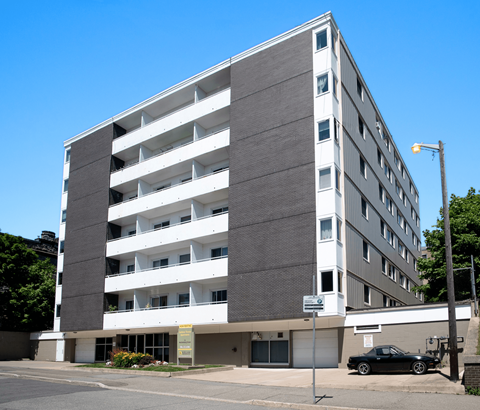 A black car is parked in front of a multi-story parking garage.
