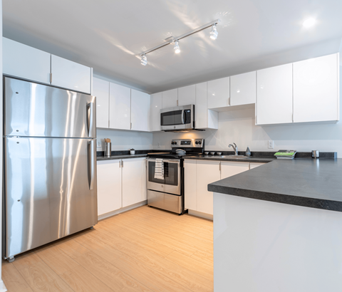 A modern kitchen with a stainless steel refrigerator and black countertops.
