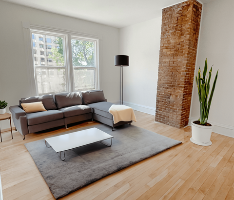 A living room with a grey couch, a white coffee table, a tall brick pillar, and a potted plant.