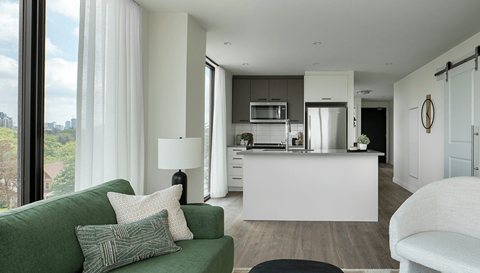 A modern living room with a green couch and a kitchen in the background.