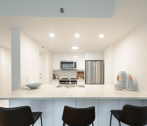 A modern kitchen with a white countertop and black chairs.