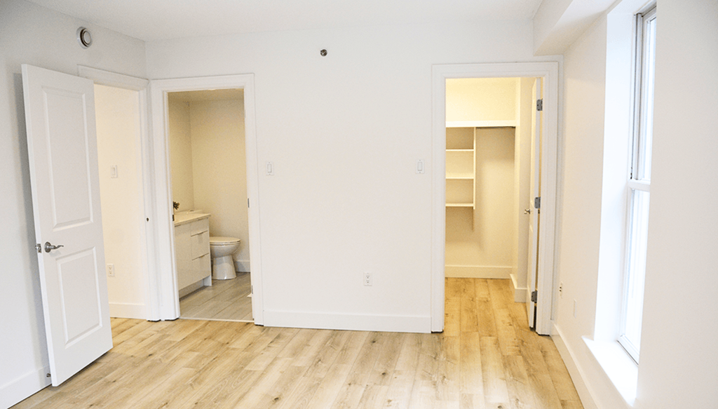 A room with white walls and wooden floors, with a toilet visible in one corner.
