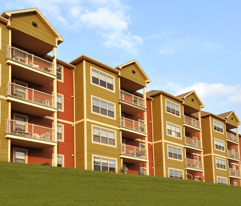 Apartment buildings with balconies and windows are lined up on a grassy hill.