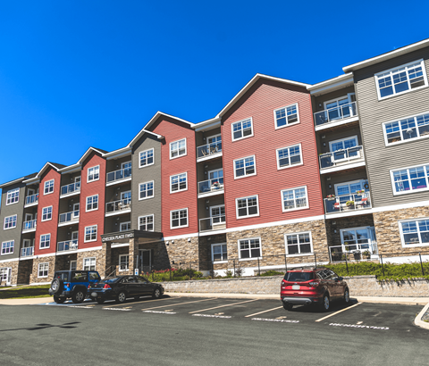 A parking lot in front of a multi-story apartment building with cars parked.