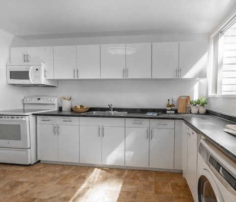 A kitchen with white cabinets and appliances, a tiled backsplash, and a wooden floor.