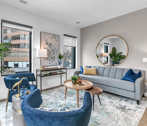 A living room with a grey couch, blue armchair, and a round mirror.