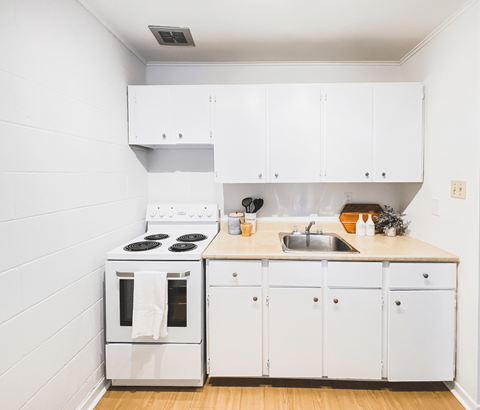 A white kitchen with a stove, sink, and cabinets.