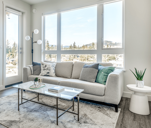 A living room with a grey couch, a glass coffee table, and a large window overlooking a snowy landscape.