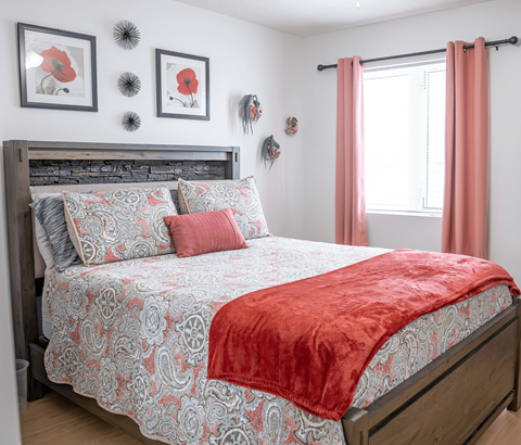A bed with a red blanket and a grey and red patterned duvet cover.