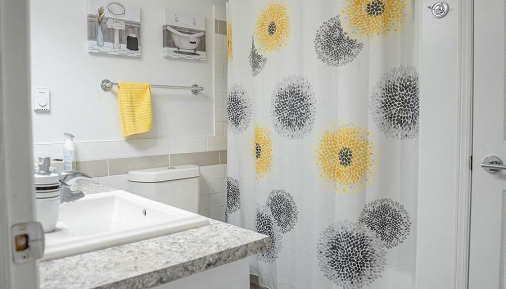 A bathroom with a sink, toilet, and a shower curtain with yellow and grey flowers.