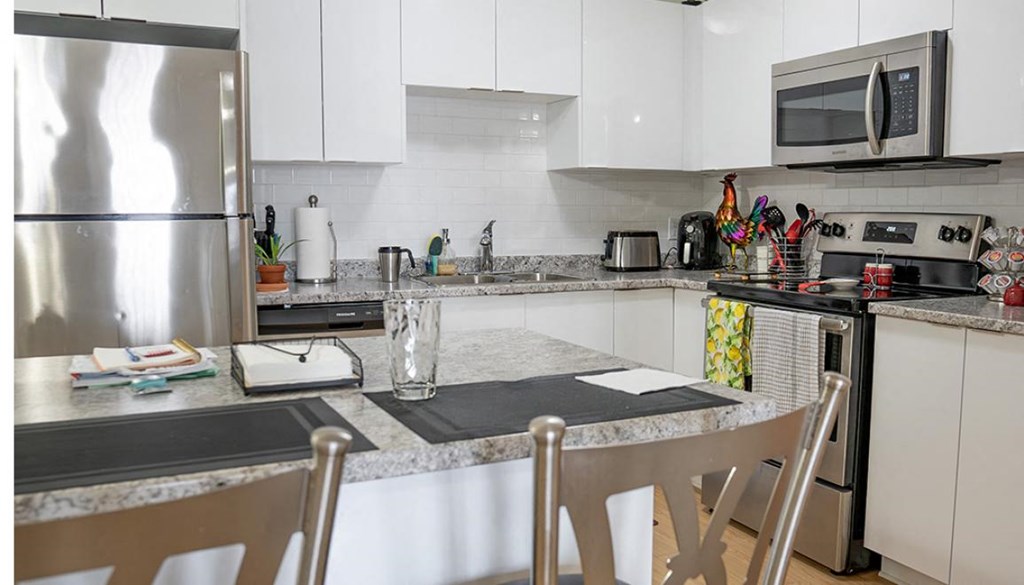 A kitchen with a table and chairs in the foreground and a refrigerator and microwave in the background.