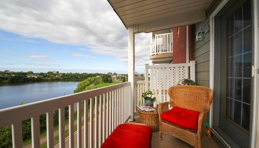 A balcony with a chair and a table overlooking a river.
