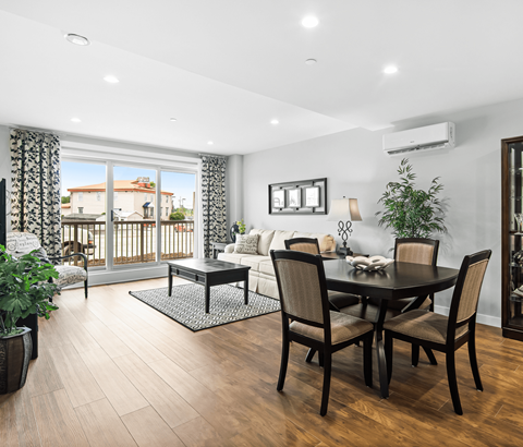 A dining room with a table set for four and a balcony with a view of a house.