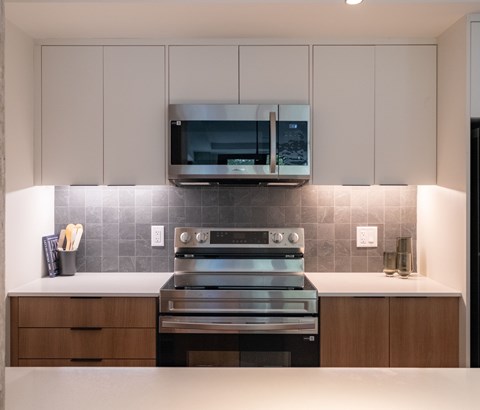 A modern kitchen with a stainless steel oven and microwave above a counter with a tiled backsplash.