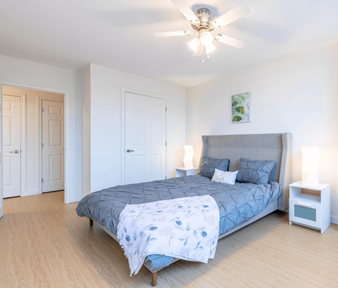A bedroom with a bed, a ceiling fan, and a nightstand.