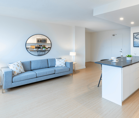 A modern living room with a grey sofa and a round mirror on the wall.